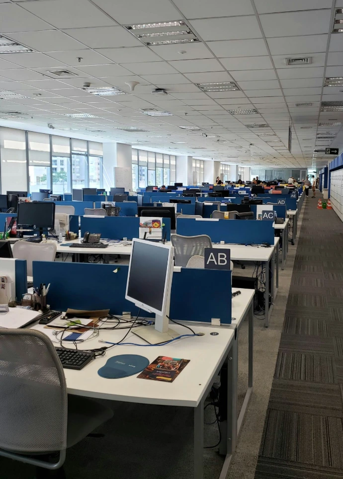 Office containing multiple rows of desks with chairs and computer monitors
